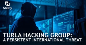 Hooded figure at computers engages in hacking activities.